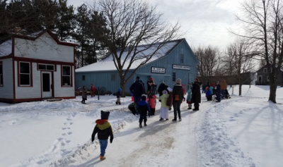 Adults and children exploring snowy trails and buildings at Pinecrest Village.