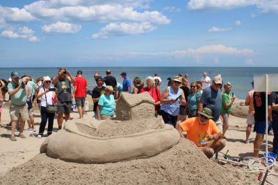 A crowd surrounding an elaborate sand sculpture on a beach.