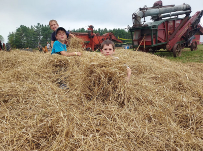 Kids playing in a big pile of hay with equipment in background.