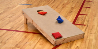 Cornhold board with three bean bags on a gym floor.